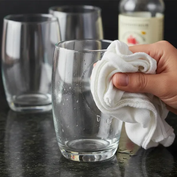 A hand wiping a cloudy glass with a vinegar-soaked cloth, showing a clear section emerging, with other cloudy glasses in the background